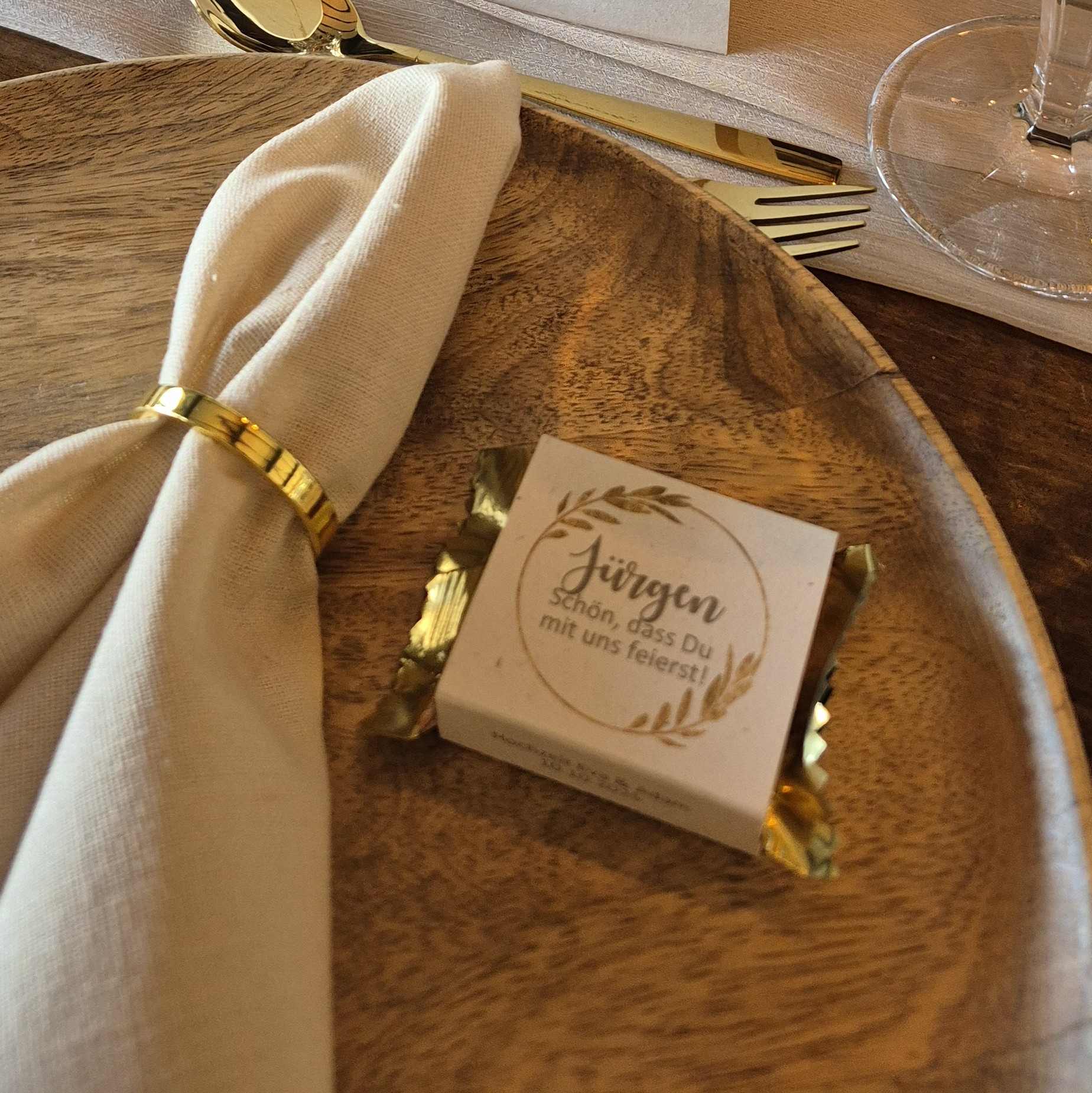 Hochzeit-Gastgeschenk-Banderole Haselnusstafel in goldener Verpackung mit Banderole und Gastnamen als Hochzeits-Gastgeschenk auf Holzteller dekoriert
